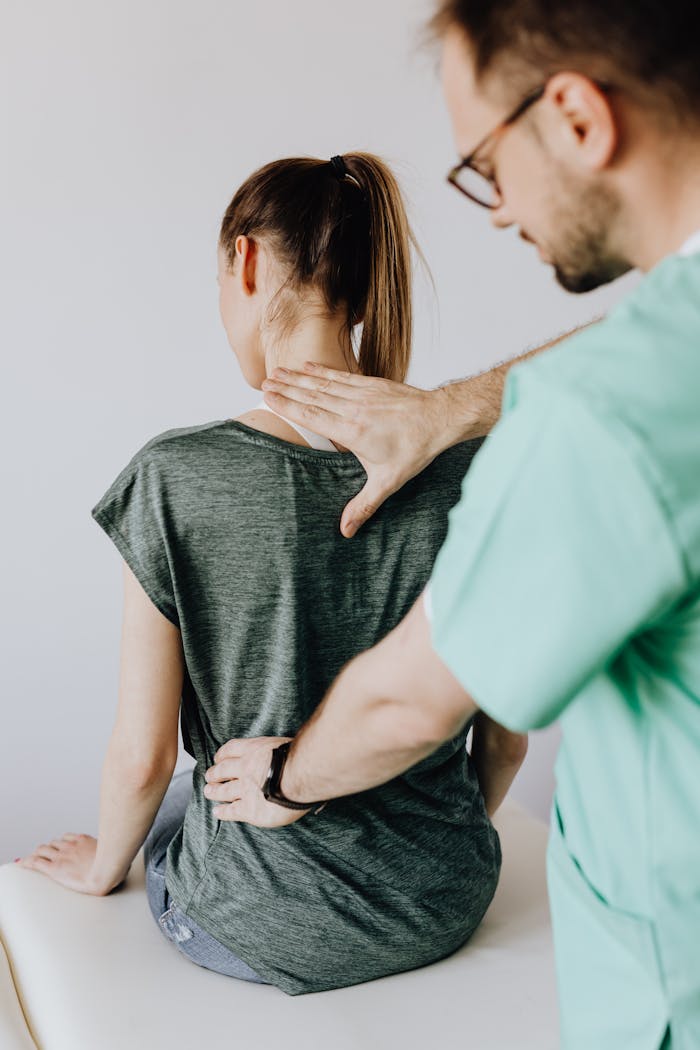 A doctor performs a spine examination on a seated patient at a medical clinic.